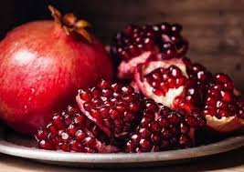ثمرة رمان كاملة بجانب قطع رمان مفتوحة تظهر حباتها الحمراء اللامعة على طبق، مما يبرز جمال الفاكهة وفوائدها الصحية.